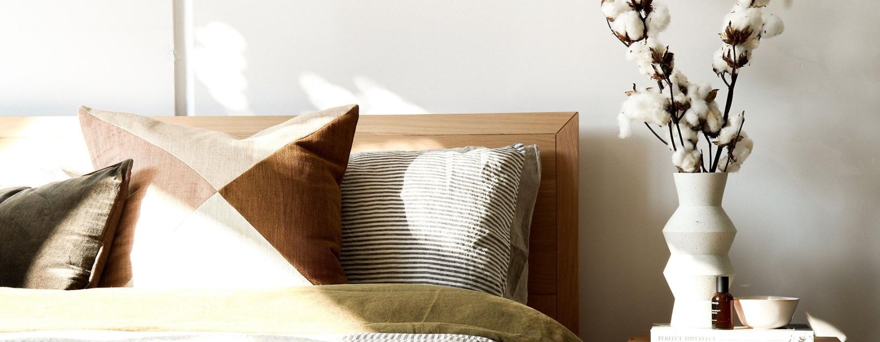 swath of sunlight shines across a well made bed and bedside table with a vase of cotton plants